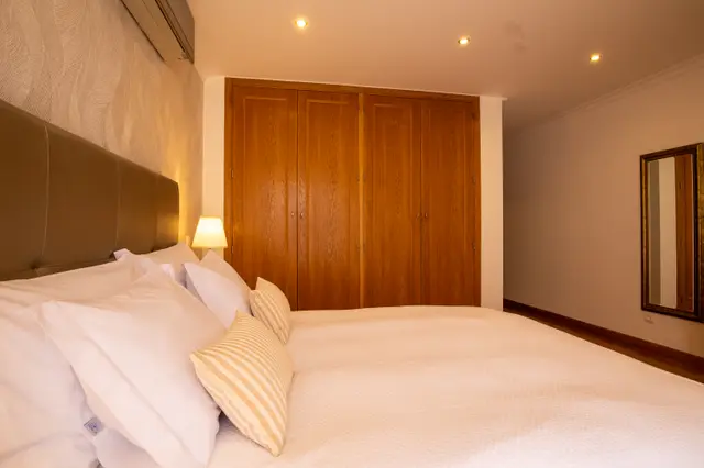 Bed and pillows facing the wooden wardrobe in the room.