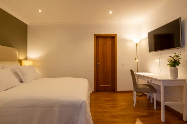 Bed foreground with desk, TV and floor lamp opposite.