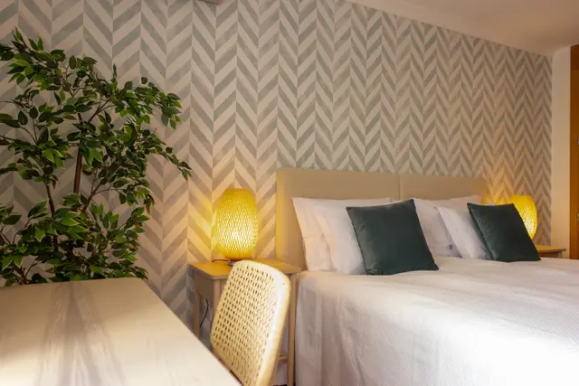Bed with bedside lamps and a desk with cane chair.