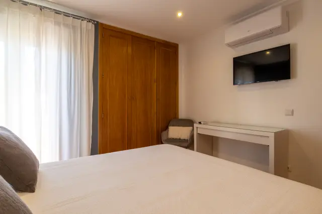 Wardrobe, desk, armchair and wall-mounted TV in the room.
