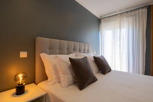 Bed head with cushions beside sheer-curtained balcony window.